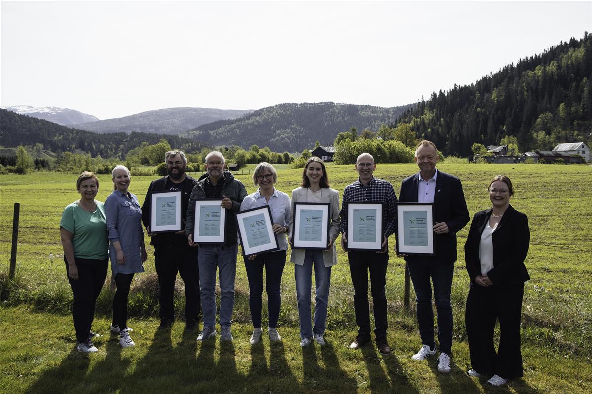 9 personar, 6 av dei viser fram diplom, på eit grønt gjorde med skogkledde fjell i bakgrunnen - Klikk for stort bilete